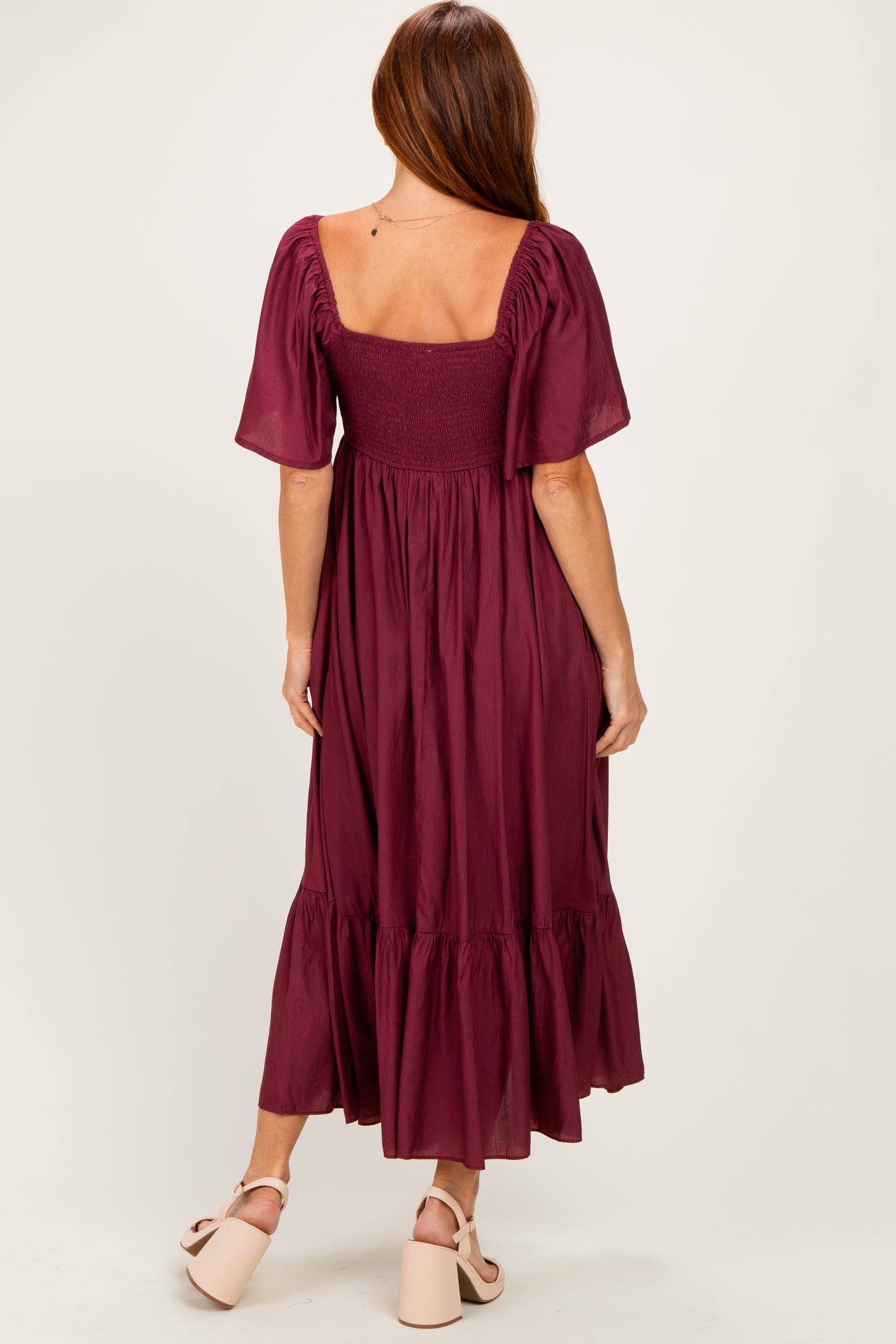 woman wearing a burgundy midi dress with puff sleeves and a smocked bodice, showing a ruffled hem at the back