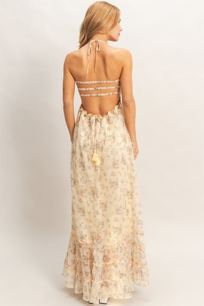 woman wearing a backless yellow floral maxi dress with ruffled hem and adjustable tie straps