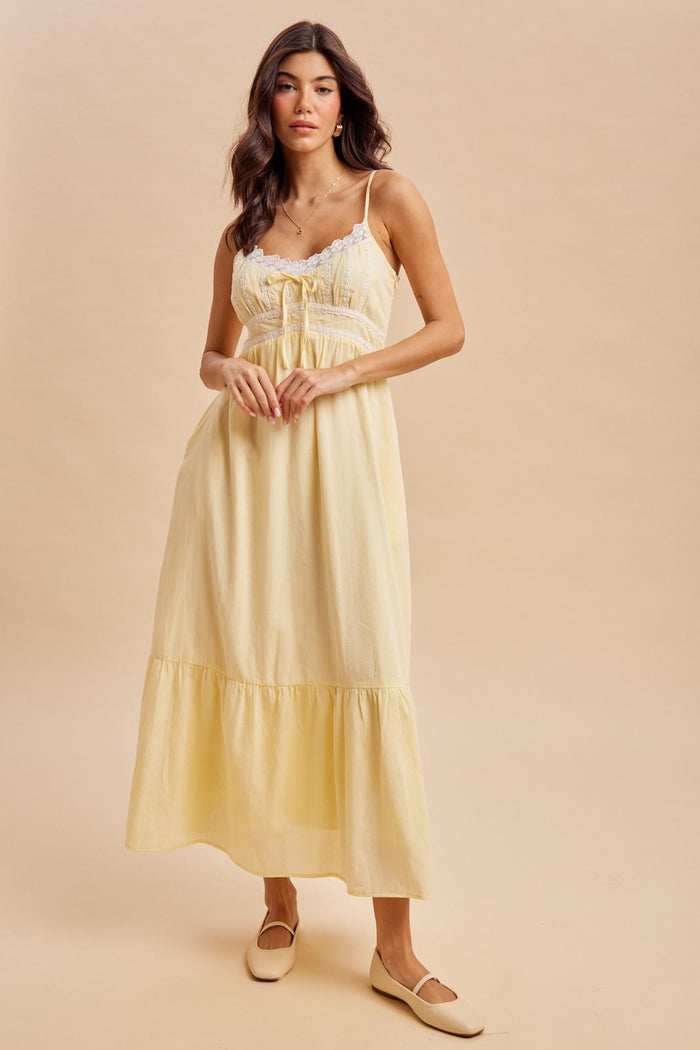 woman wearing a yellow maxi dress with lace detailing and a tiered skirt, standing against a neutral background