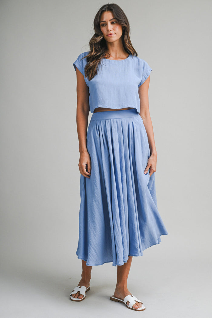 woman wearing a light blue cropped top and matching flowing midi skirt with sandals