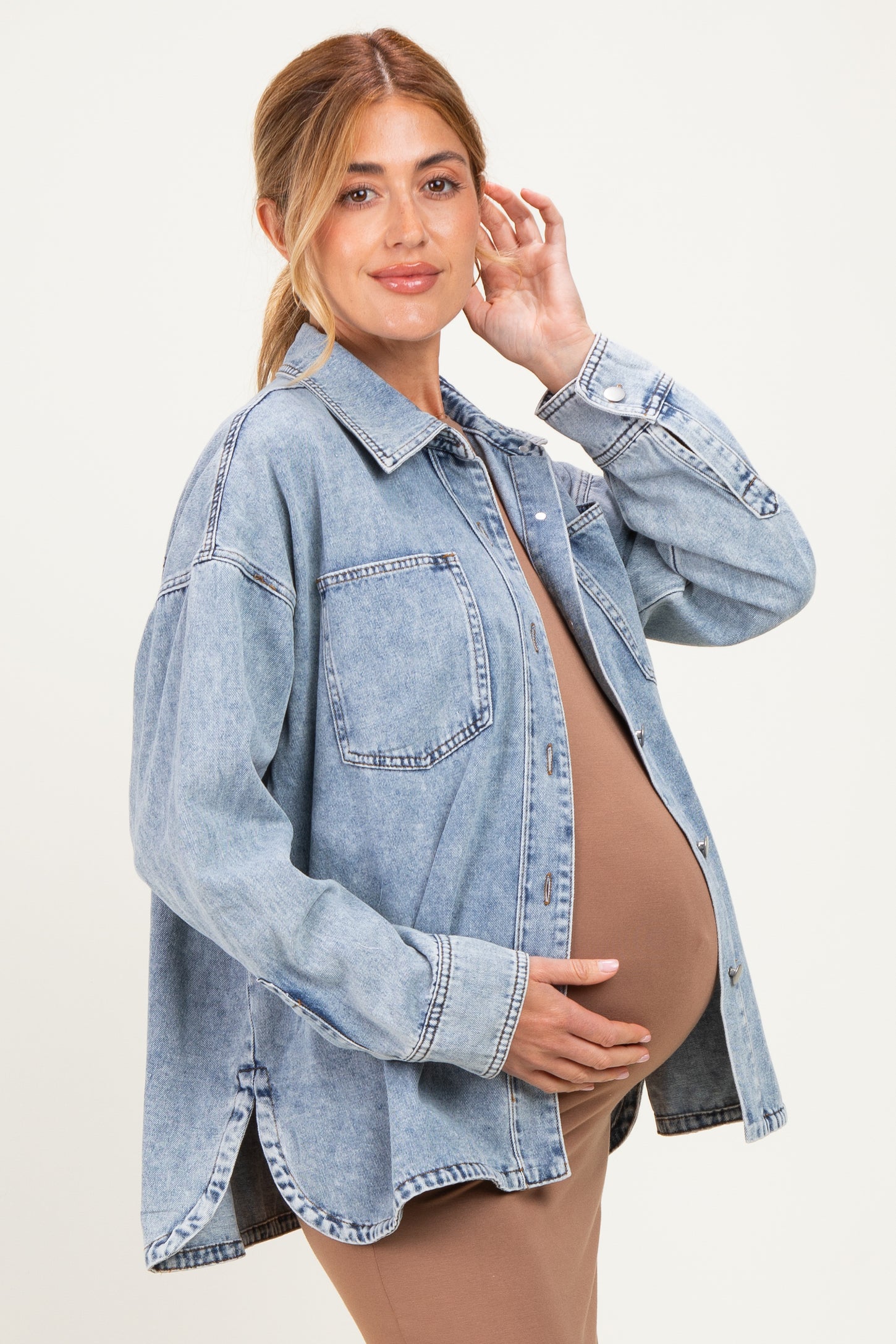 woman wearing a light blue oversized denim jacket, showcasing her baby bump in a fitted brown dress underneath