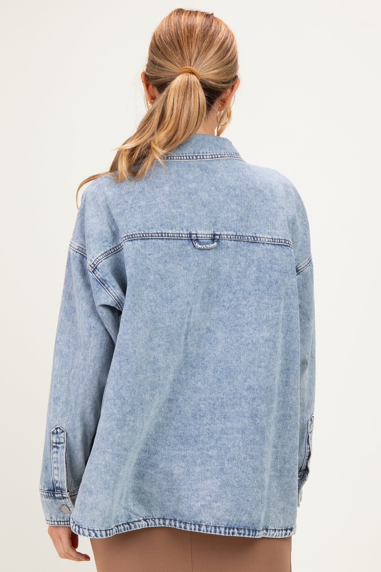 woman wearing a light blue oversized denim jacket, styled with a casual look, showing the back view