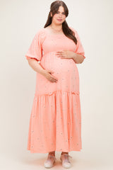 woman wearing a coral maternity dress with short puff sleeves and tiered skirt, holding her baby bump