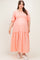 woman wearing a coral pink maternity plus maxi dress with puff sleeves and embroidered details, featuring a baby bump