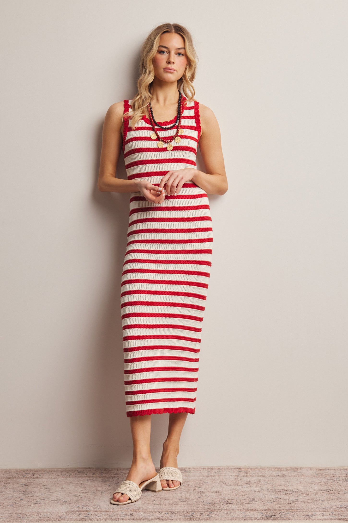 woman wearing a red and white striped midi dress with a sleeveless design and a ruffled hem, standing against a wall