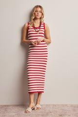 woman wearing a red and white striped midi dress with a sleeveless design and a ruffled hem, standing against a wall