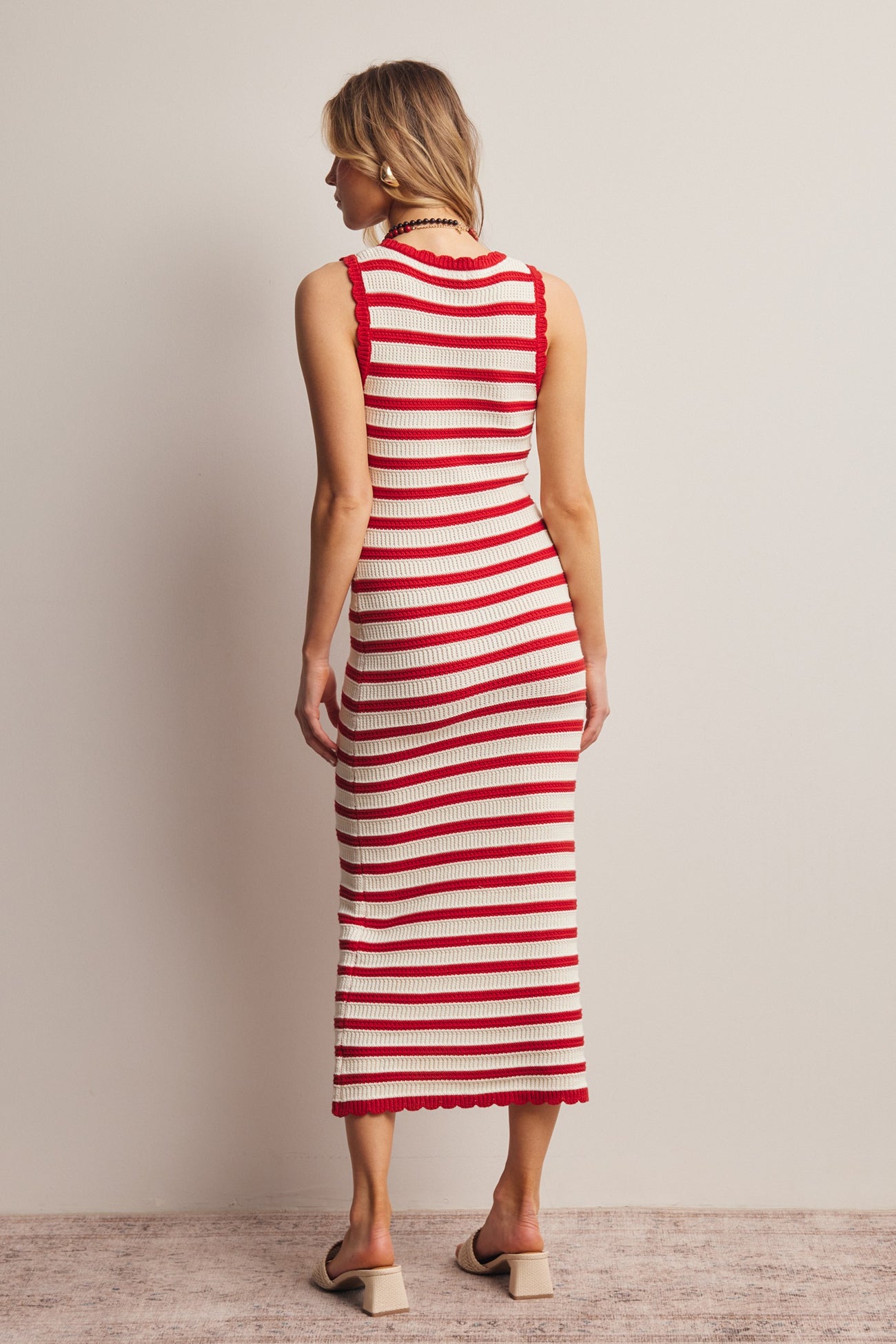 woman wearing a red and cream striped knit midi dress with a fitted silhouette and scalloped hem details, viewed from the back