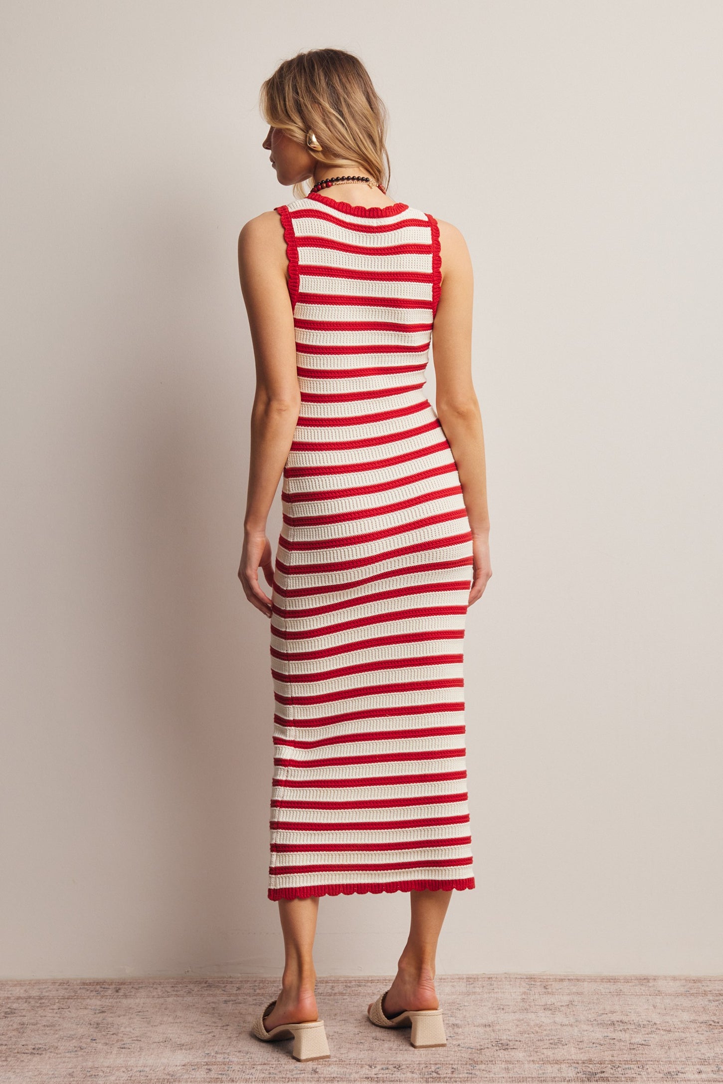 woman wearing a red and cream striped knit midi dress with a fitted silhouette and scalloped hem details, viewed from the back