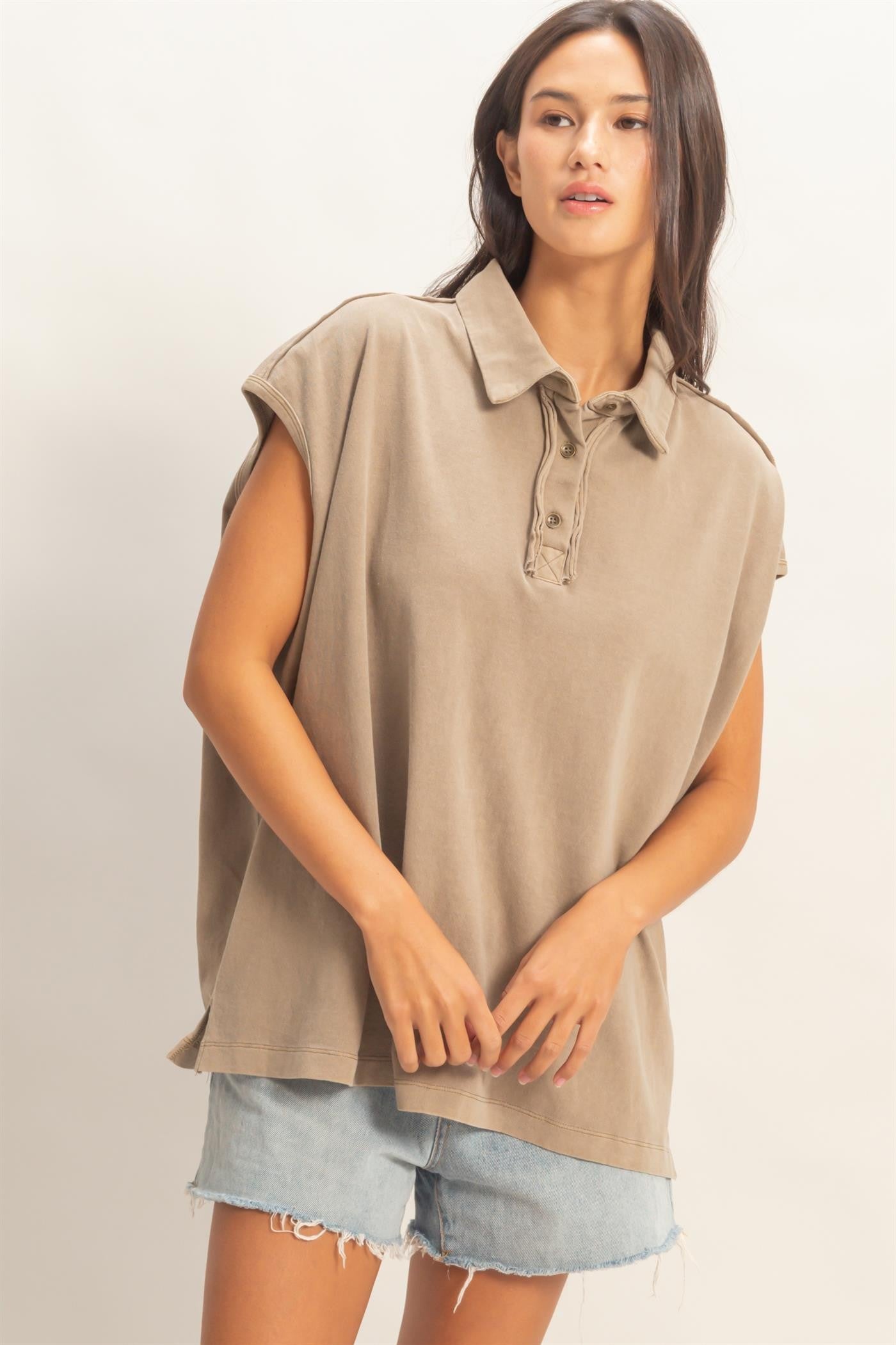 woman wearing a taupe oversized polo shirt with short sleeves, paired with light blue denim shorts
