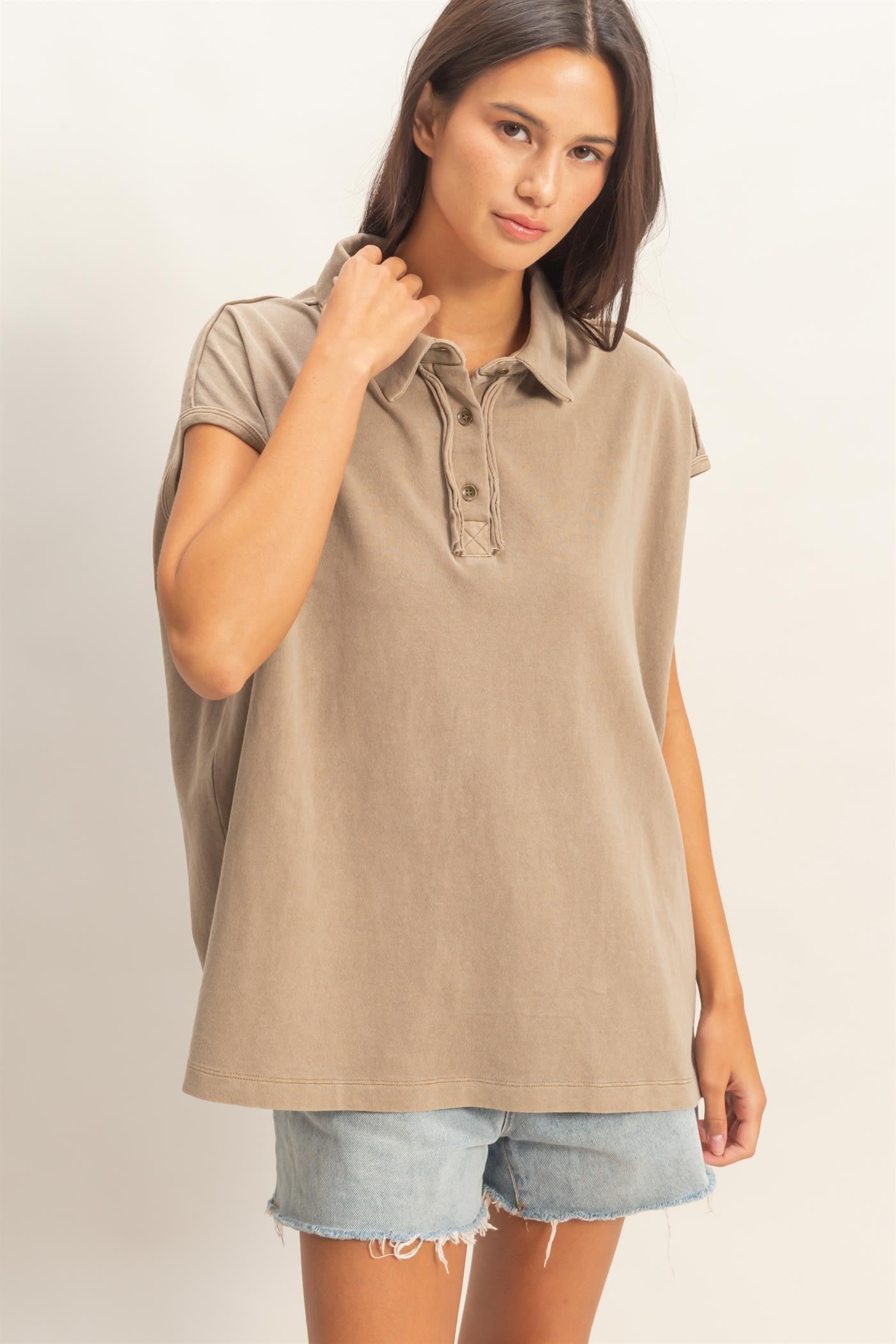 woman wearing a taupe oversized polo shirt with short sleeves and denim shorts