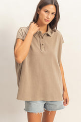 woman wearing a taupe oversized polo shirt with short sleeves and denim shorts