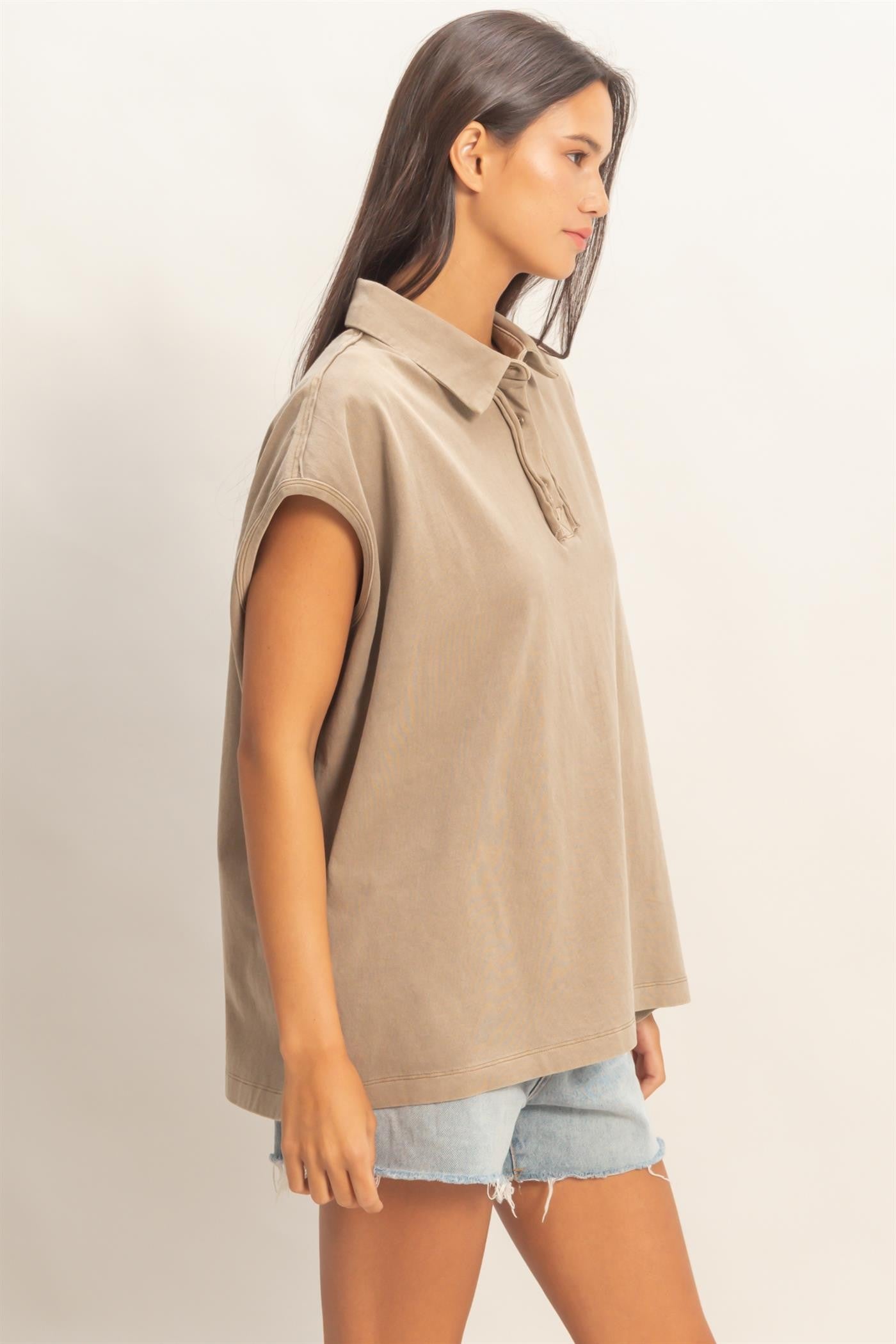 woman wearing a taupe oversized polo shirt with a collar and rolled sleeves, paired with denim shorts