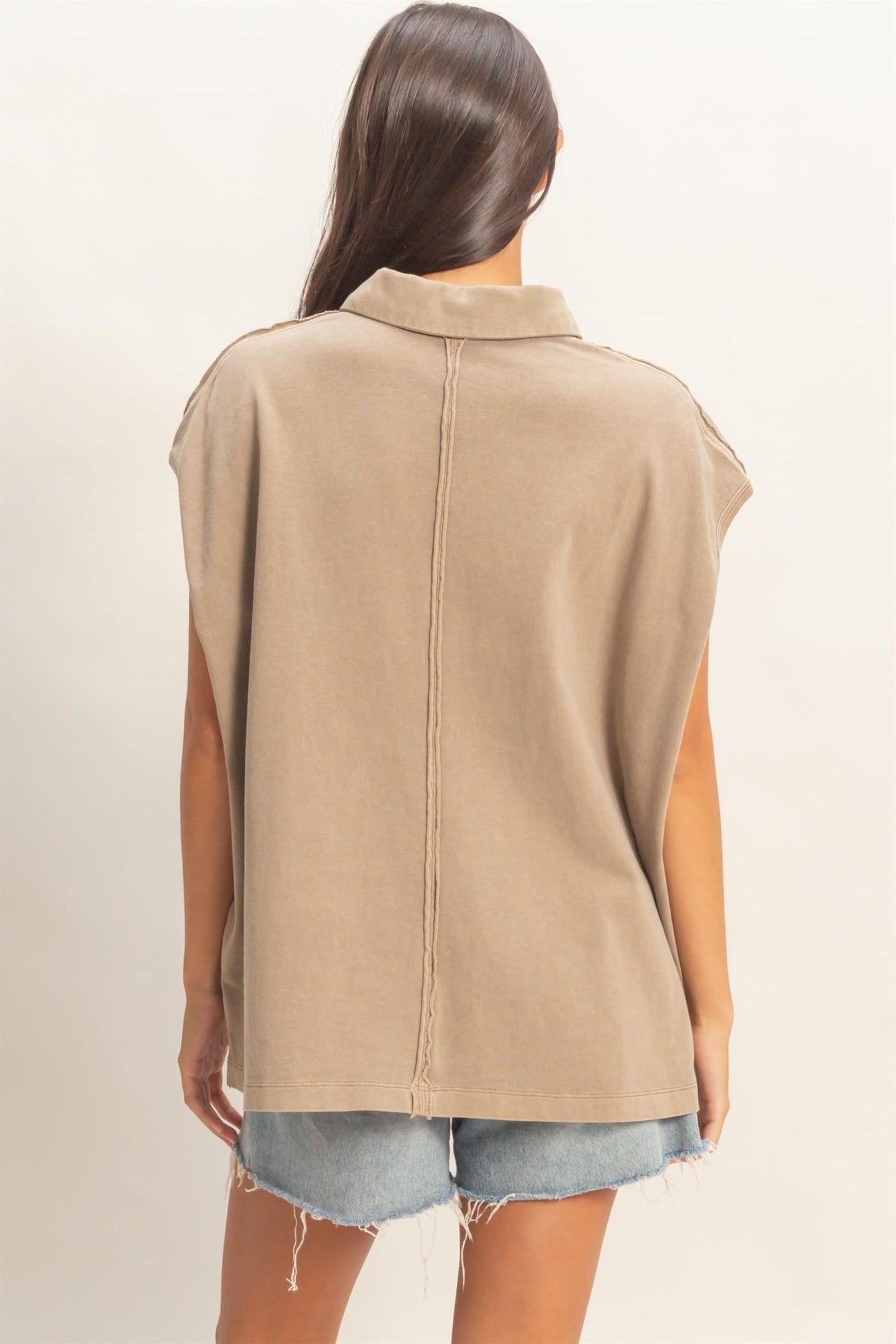 woman wearing a khaki oversized sleeveless top with a relaxed fit and stitched details, paired with denim shorts