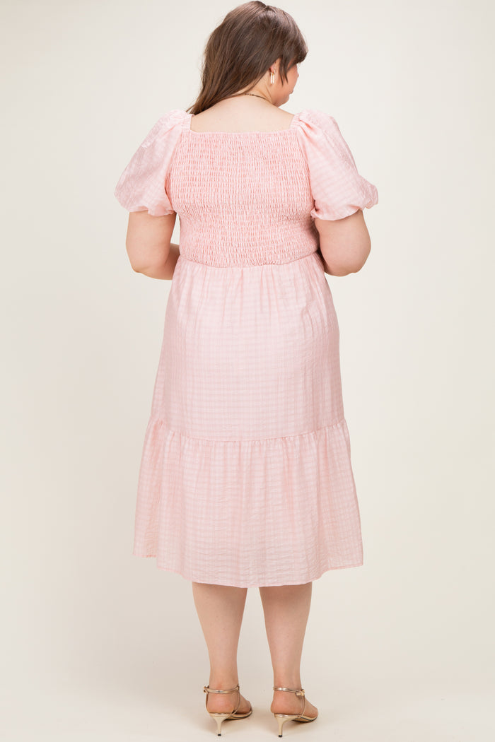 woman wearing a pink checkered smocked maternity dress with puff sleeves and a tiered hem, viewed from the back