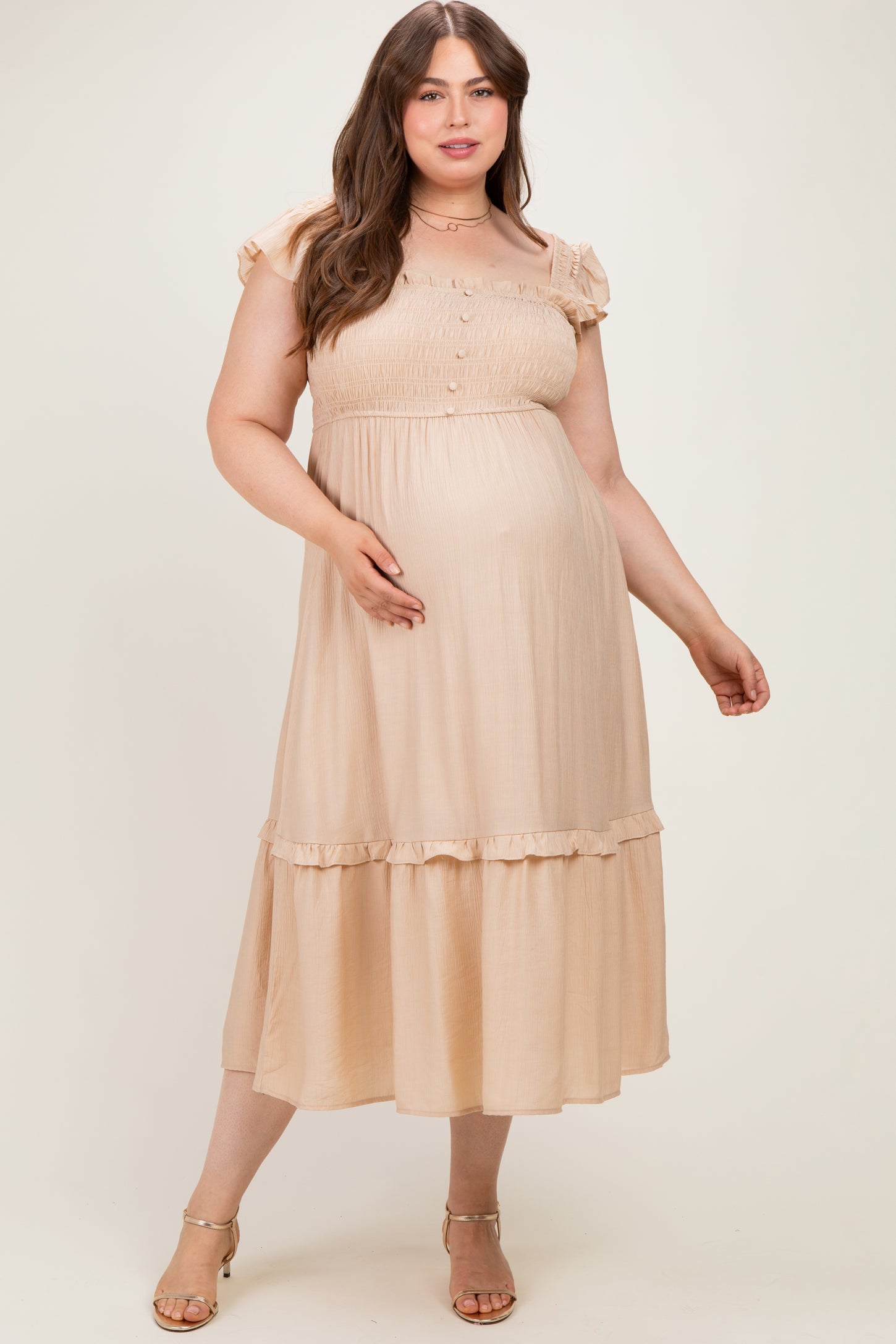 woman wearing a beige maternity plus dress with ruffle sleeves and button details, showcasing her baby bump
