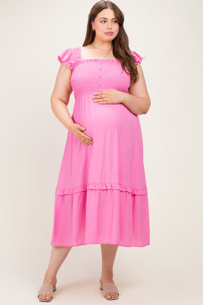 woman wearing a pink maternity plus dress with smocked bodice and ruffled sleeves, holding her baby bump