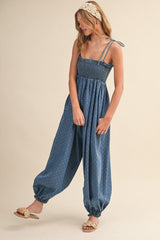 woman wearing a blue smocked jumpsuit with polka dots and adjustable straps, styled with flat sandals and a headband