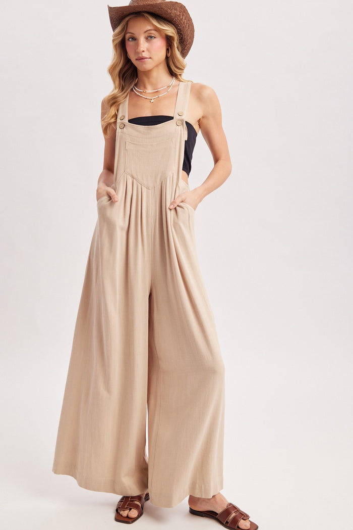 woman wearing a beige wide-leg overall jumpsuit with pockets and a black top, accessorized with a brown cowboy hat