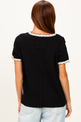 woman wearing a black short sleeve top with scalloped white trim and a relaxed fit, viewed from the back