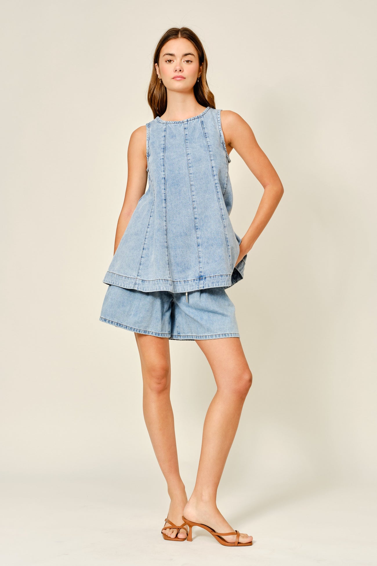 woman wearing a light blue denim sleeveless top and matching denim shorts, standing on a neutral background