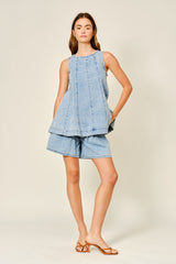 woman wearing a light blue denim sleeveless top and matching denim shorts, standing on a neutral background