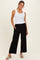 woman wearing a white ribbed tank top and black wide-leg pants, posed with one hand in pocket