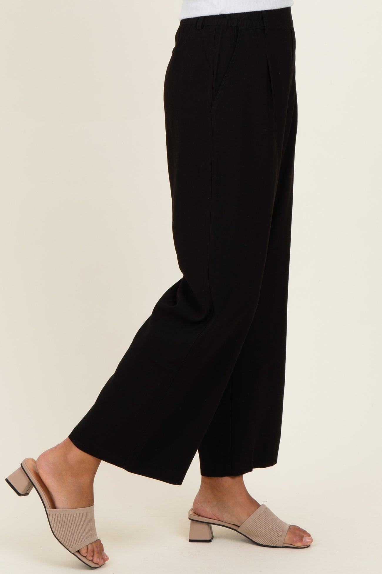 woman wearing black wide-leg trousers with pockets and beige slide sandals