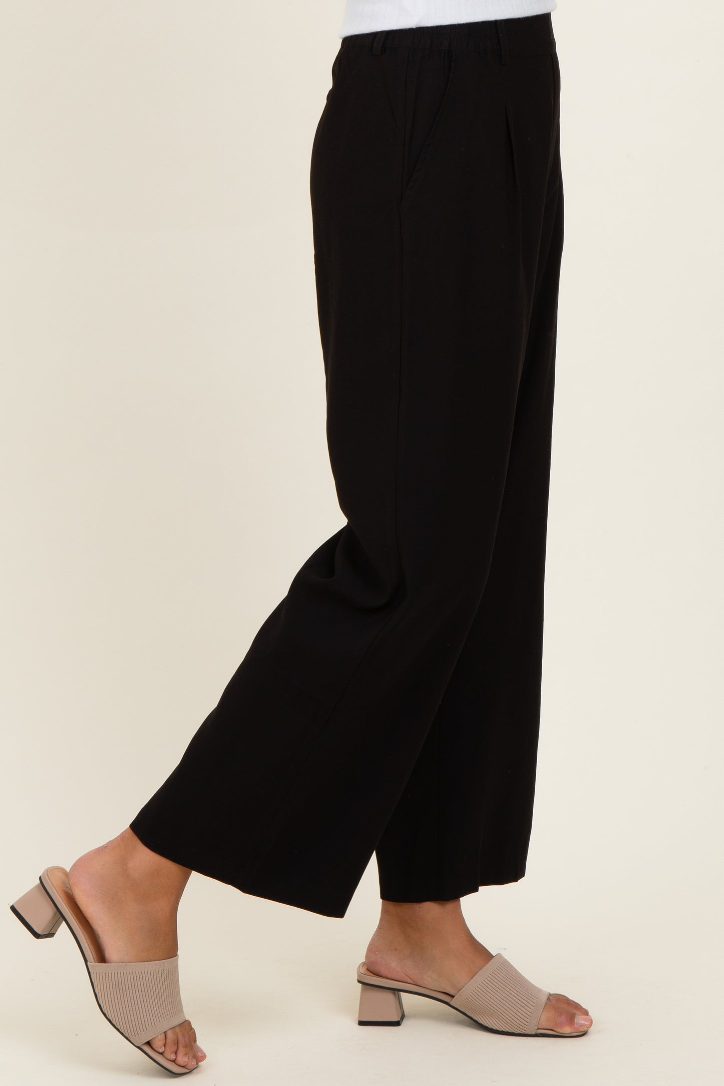 woman wearing black wide-leg trousers with pockets and beige slide sandals
