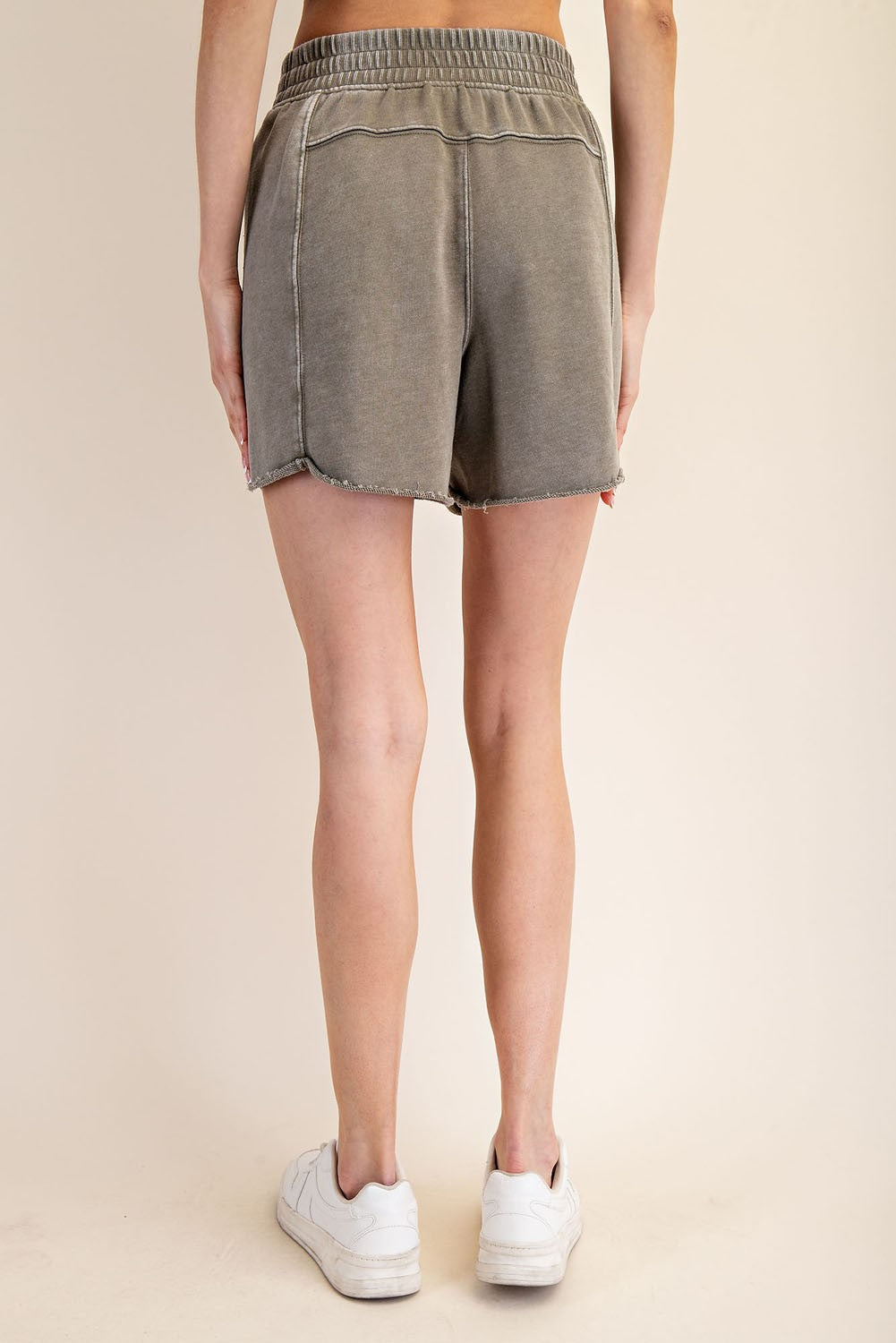 woman wearing olive green denim shorts with a frayed hem and elastic waistband, viewed from the back