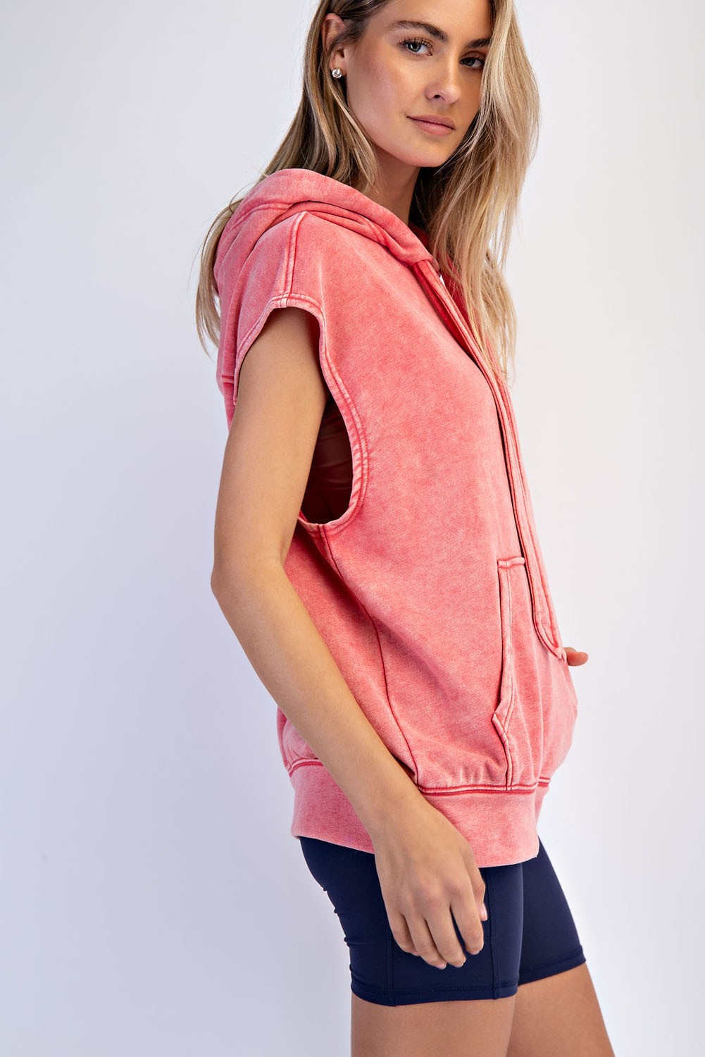 woman wearing a coral sleeveless hoodie with a front zipper, paired with navy bike shorts