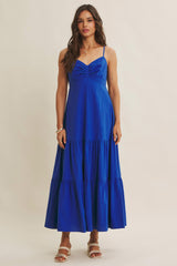 woman wearing a royal blue maxi dress with a fitted bodice and tiered skirt, standing against a plain background