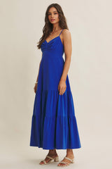 woman wearing a blue sleeveless maxi dress with a ruched bodice and tiered skirt, standing on a neutral background