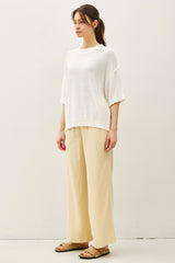woman wearing a white oversized knit sweater and beige wide-leg trousers, standing against a plain background