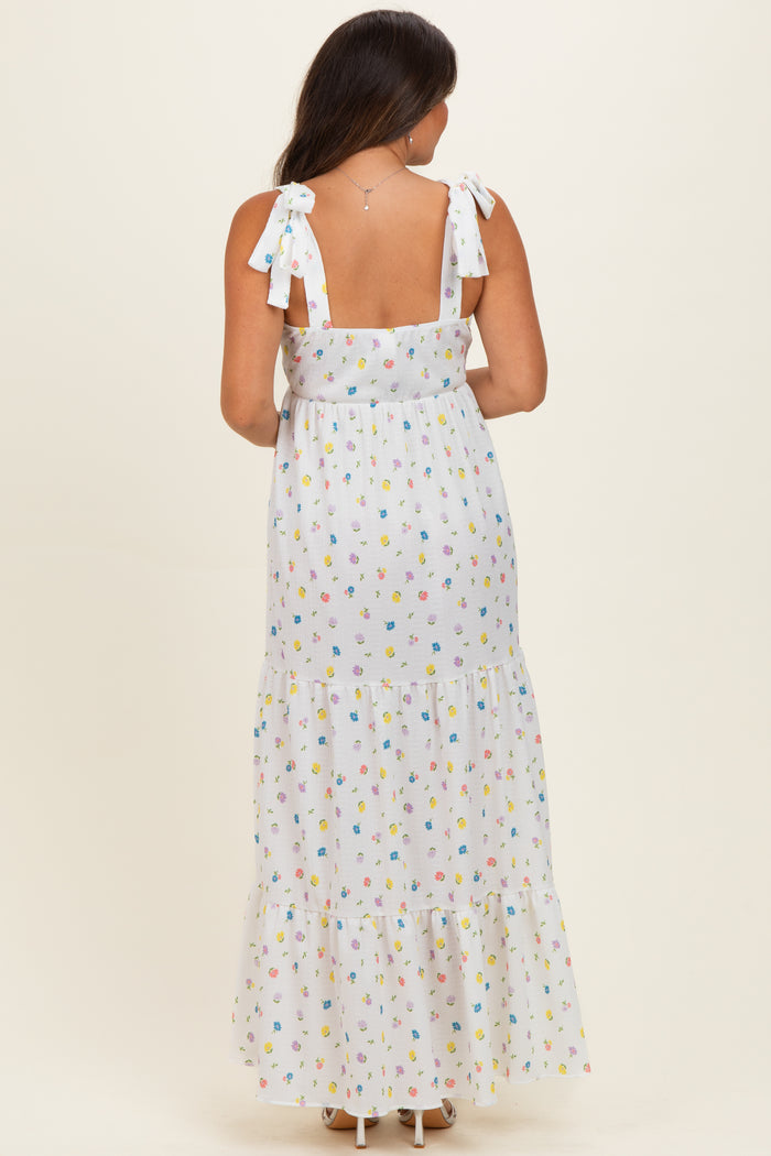 woman wearing a white maternity maxi dress with colorful floral patterns and tie shoulder straps, showing her baby bump