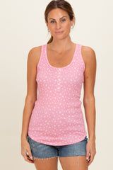 woman wearing a pink sleeveless tank top with a floral pattern and button details, paired with denim shorts