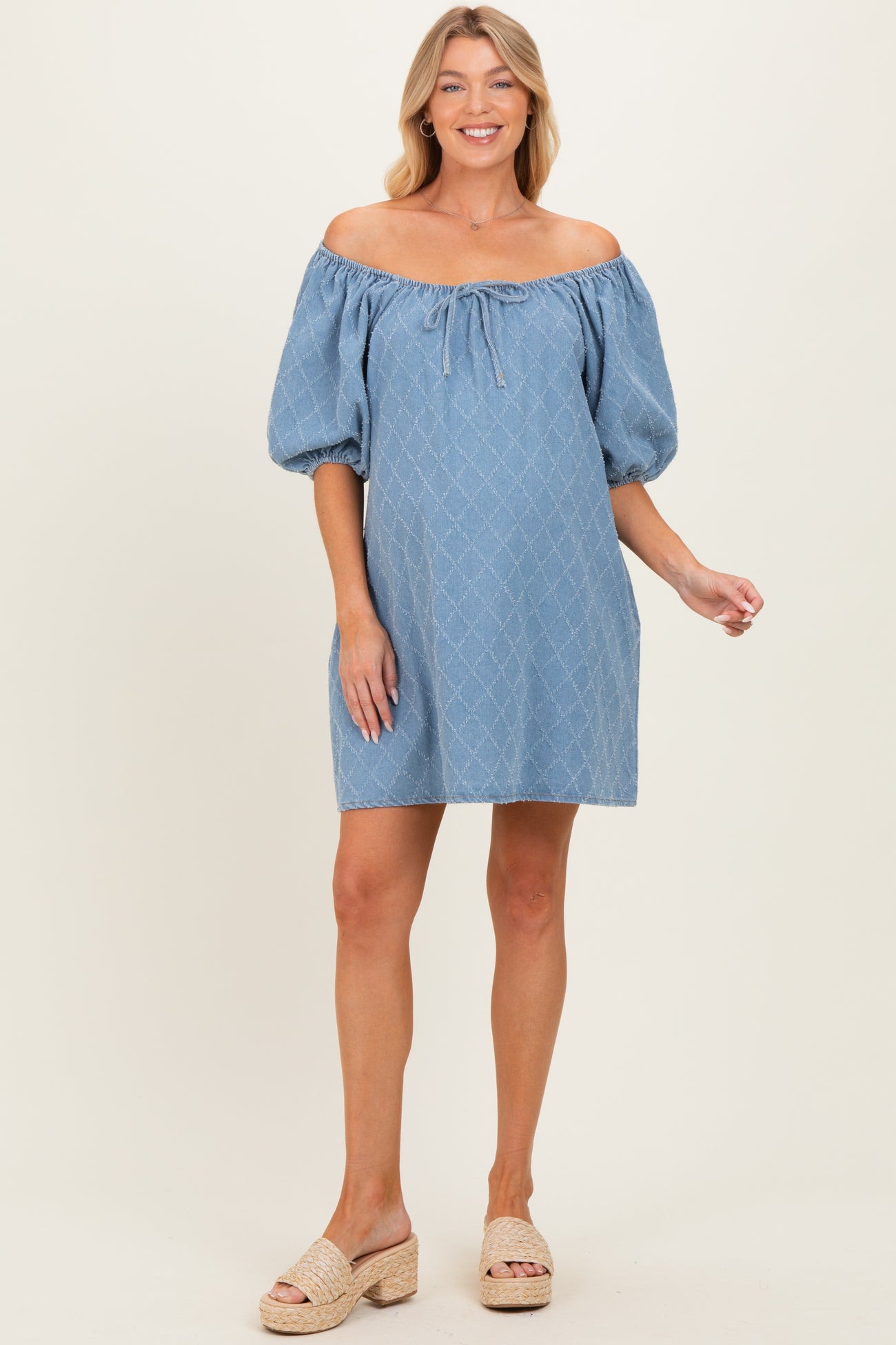 woman wearing a light blue off-the-shoulder maternity dress with puff sleeves and a tie detail