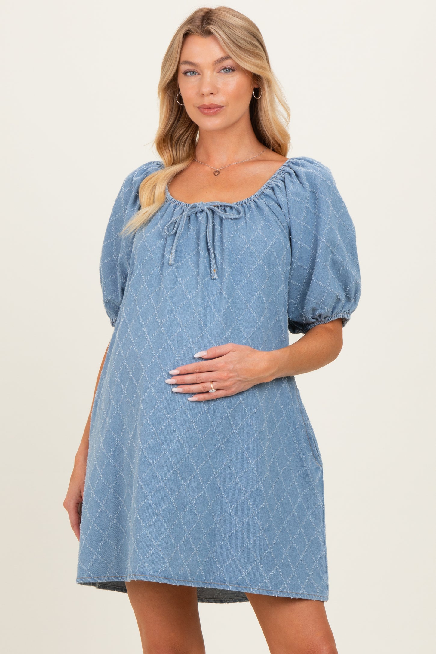 woman wearing a light blue short puff sleeve maternity dress with a scoop neckline and holding her baby bump