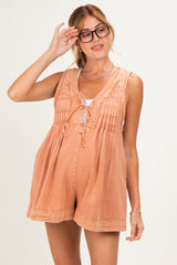 woman wearing a peach colored maternity romper with pleats and tie detail, smiling and adjusting her glasses