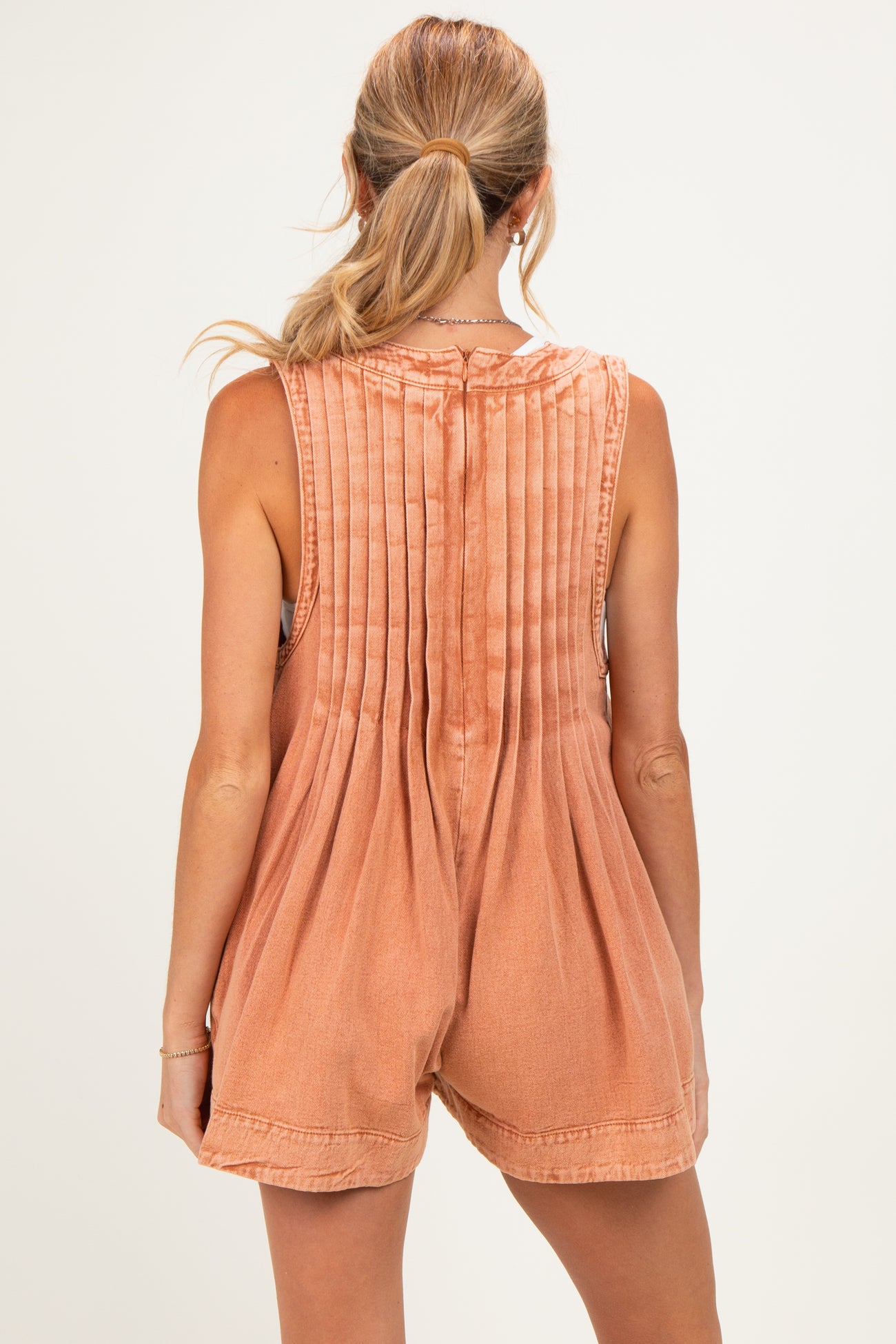 woman wearing a rust-colored maternity romper with pleated back detail