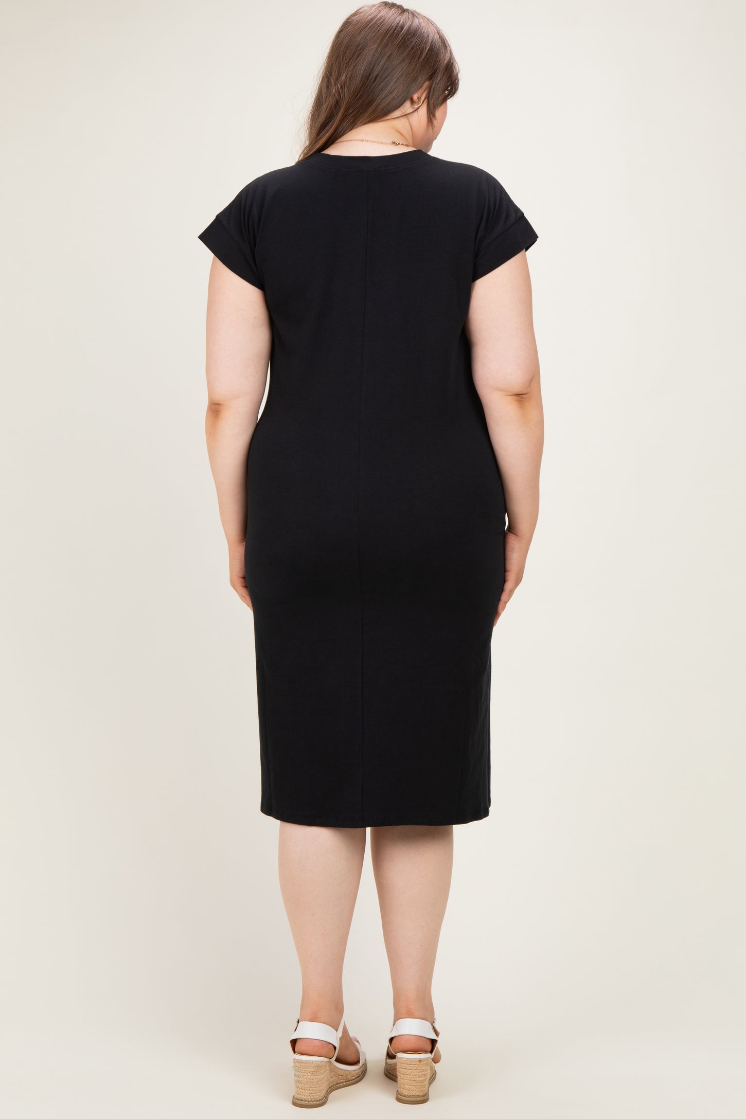 woman wearing a black maternity plus dress with cap sleeves and knee-length cut, showing the back view