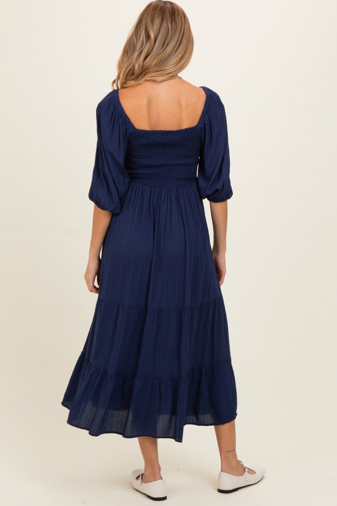 woman wearing a navy blue maternity dress with a smocked bodice and tiered skirt, viewed from the back