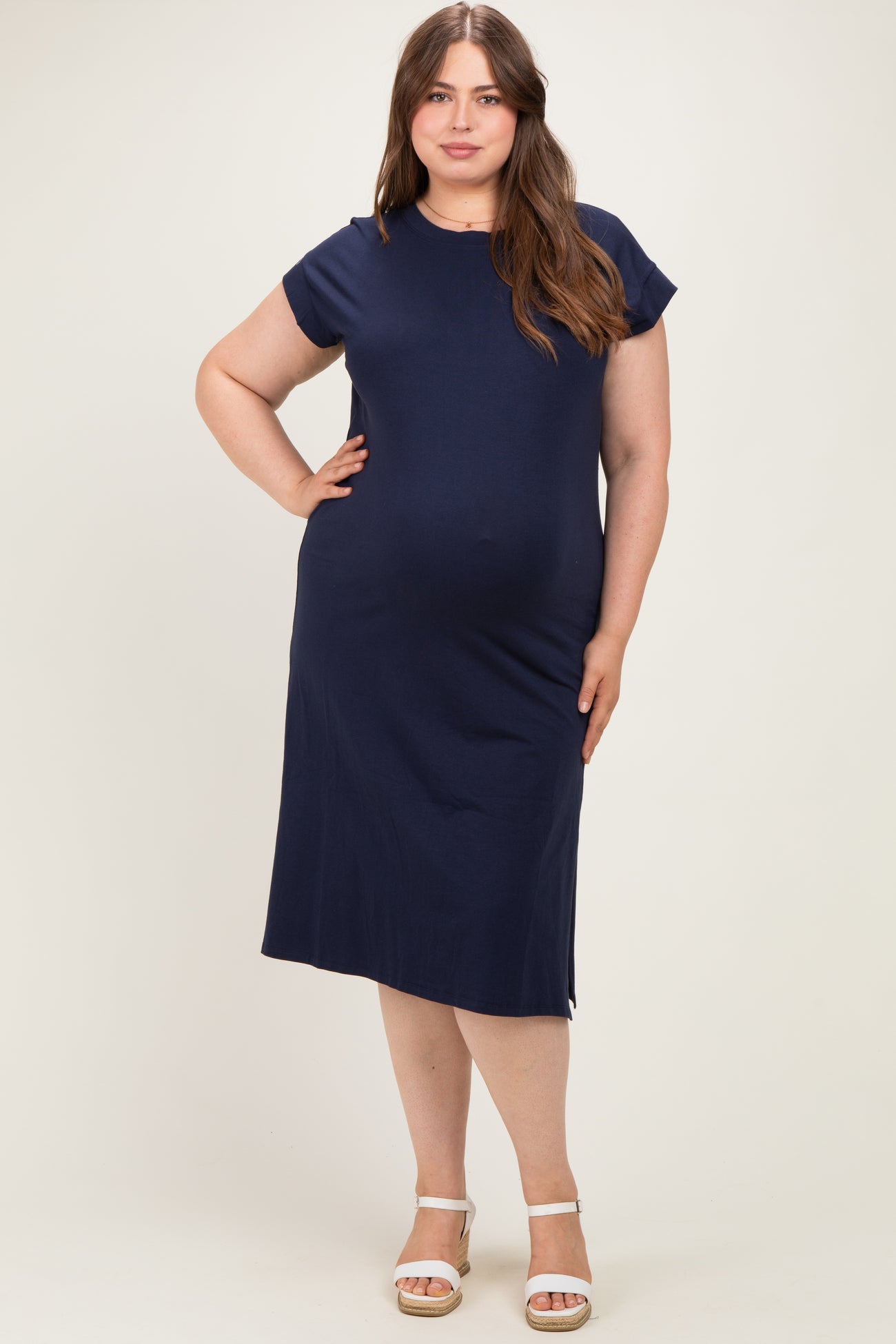 woman wearing a navy blue maternity plus dress with short cap sleeves and a relaxed fit, showcasing her baby bump