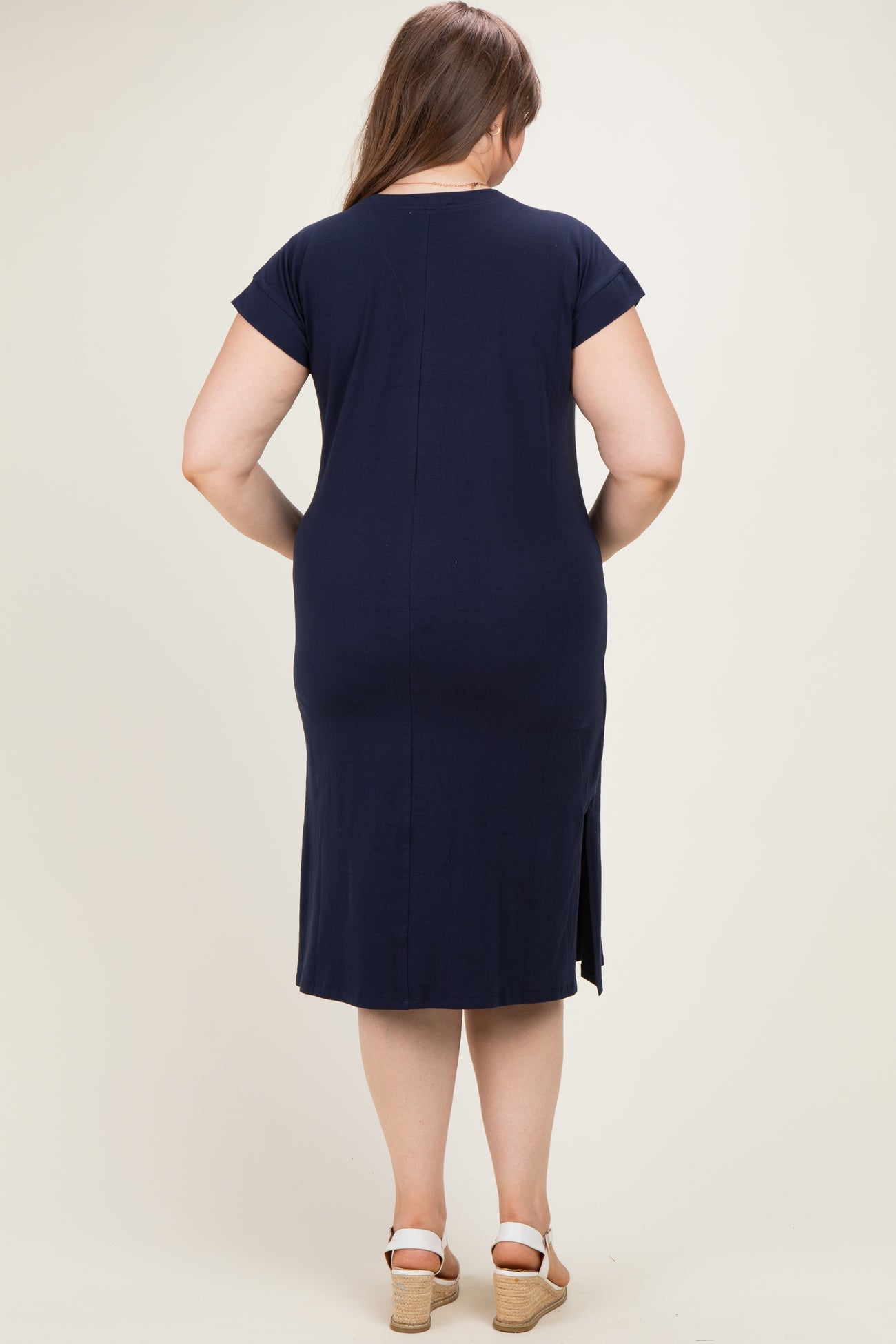 woman wearing a dark navy maternity plus dress with short sleeves and a side slit, showing her back