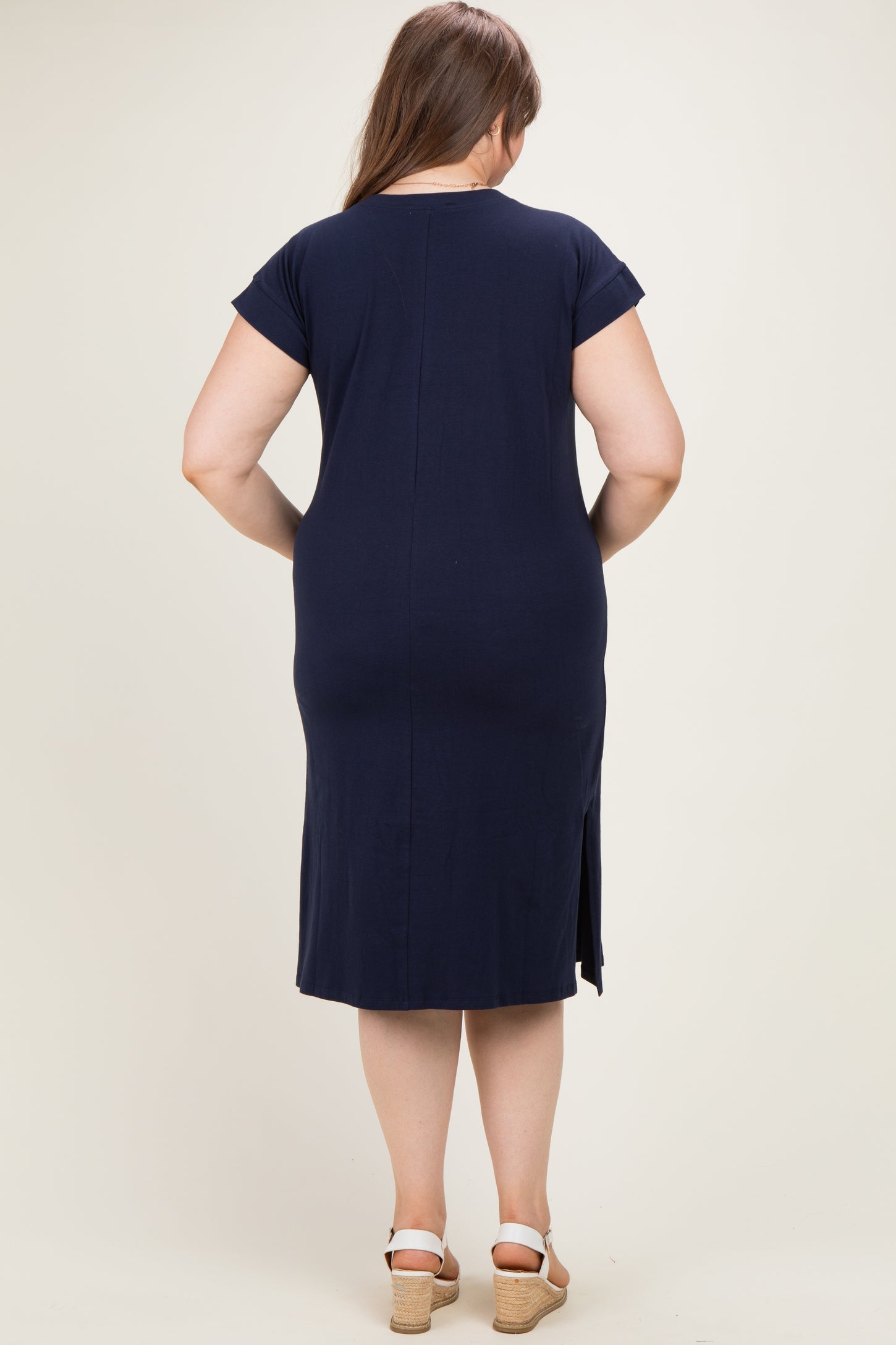 woman wearing a dark navy maternity plus dress with short sleeves and a side slit, showing her back