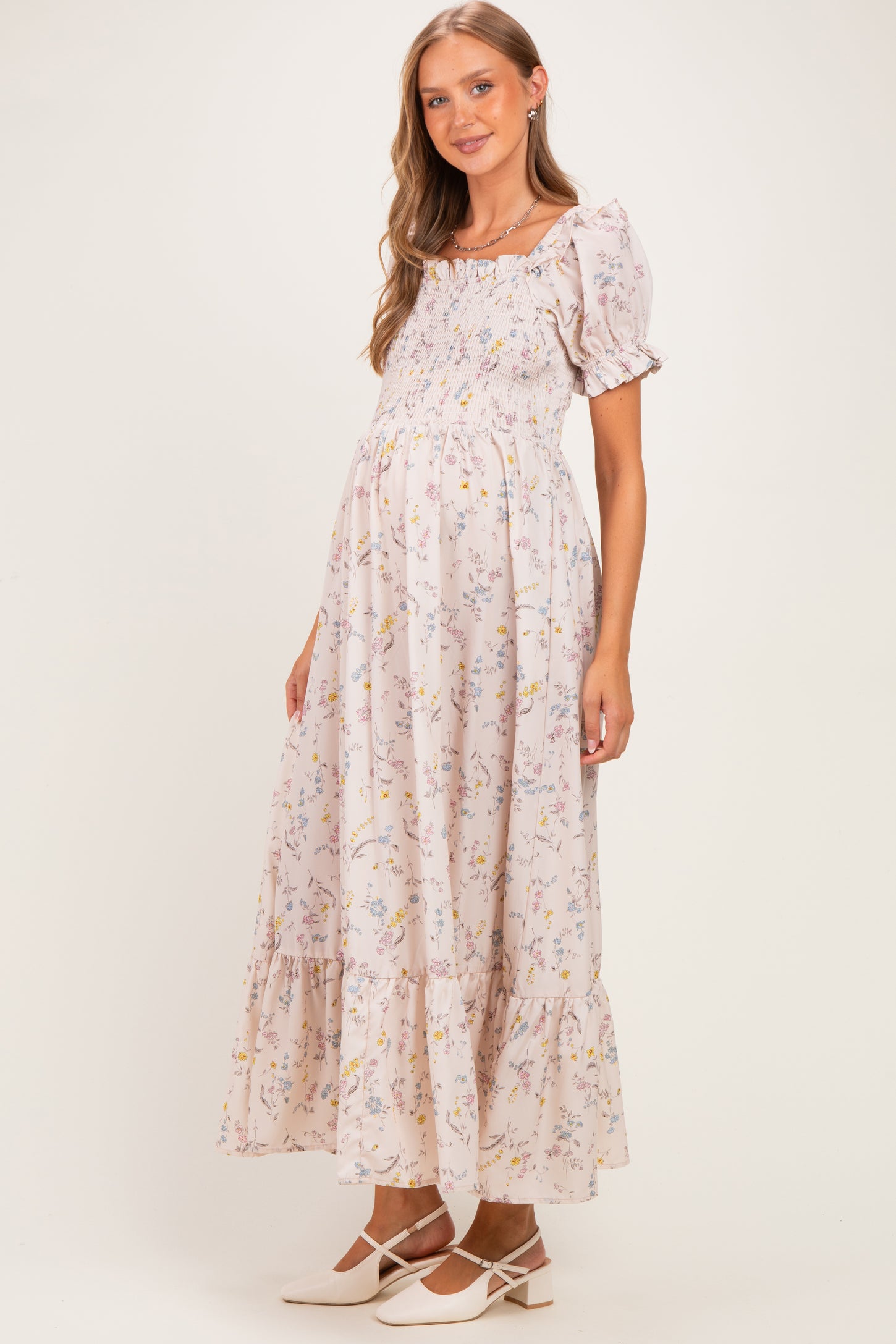 woman wearing a light pink floral maternity dress with short puff sleeves and a flowing maxi skirt, showing her baby bump