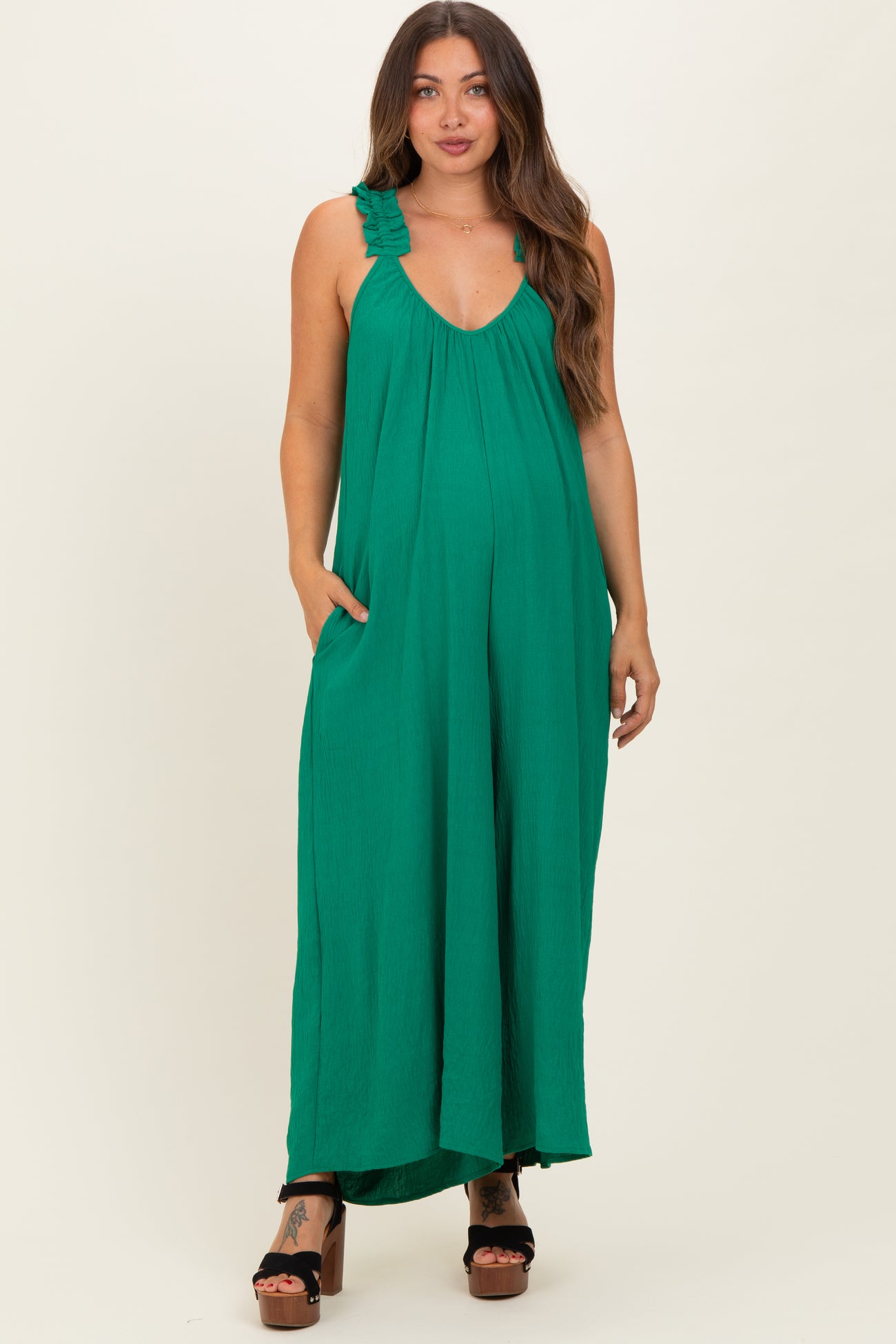 woman wearing a green maternity maxi dress with ruffle straps and pockets, showcasing her baby bump