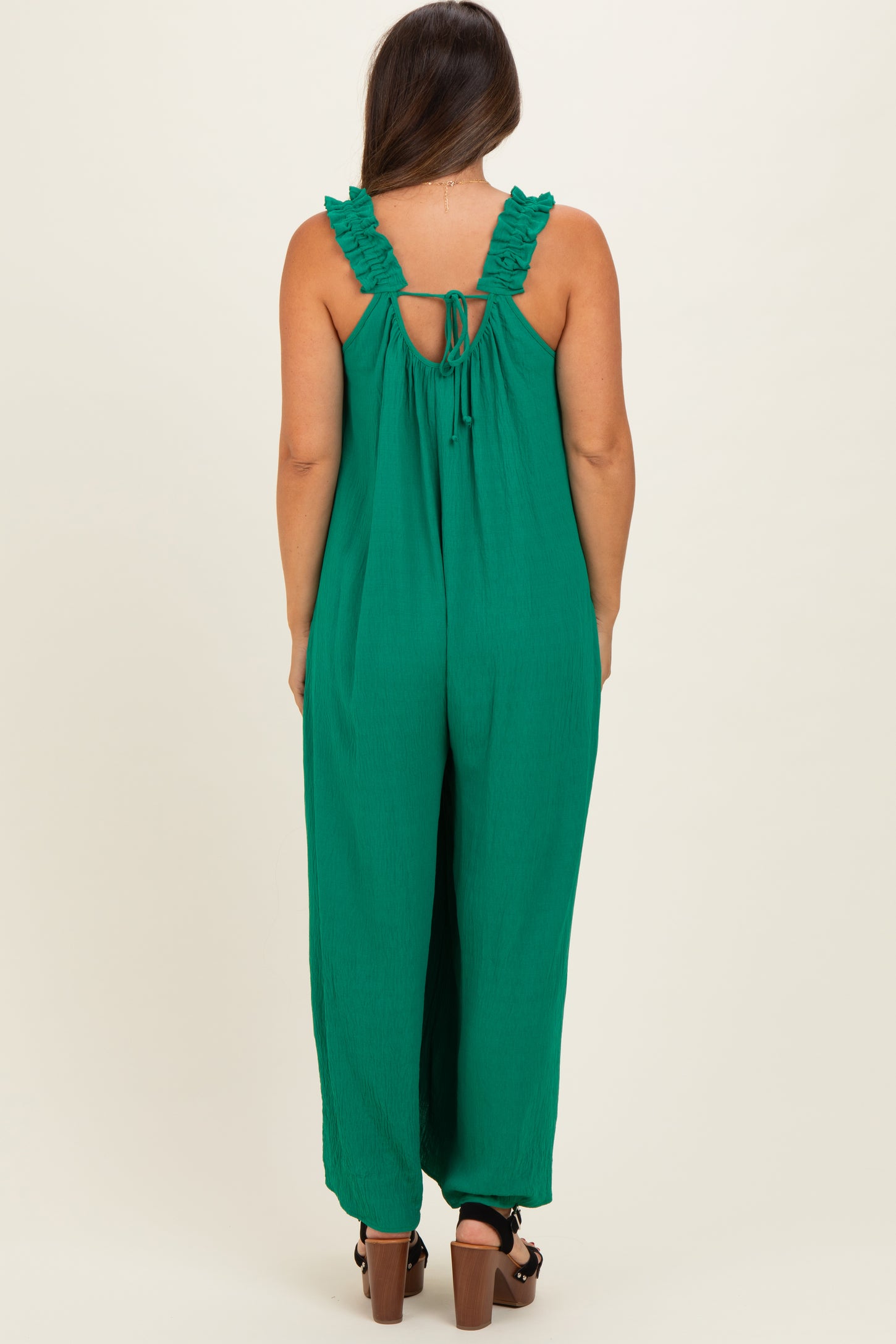 woman wearing a green maternity jumpsuit with ruffle straps and a back tie detail
