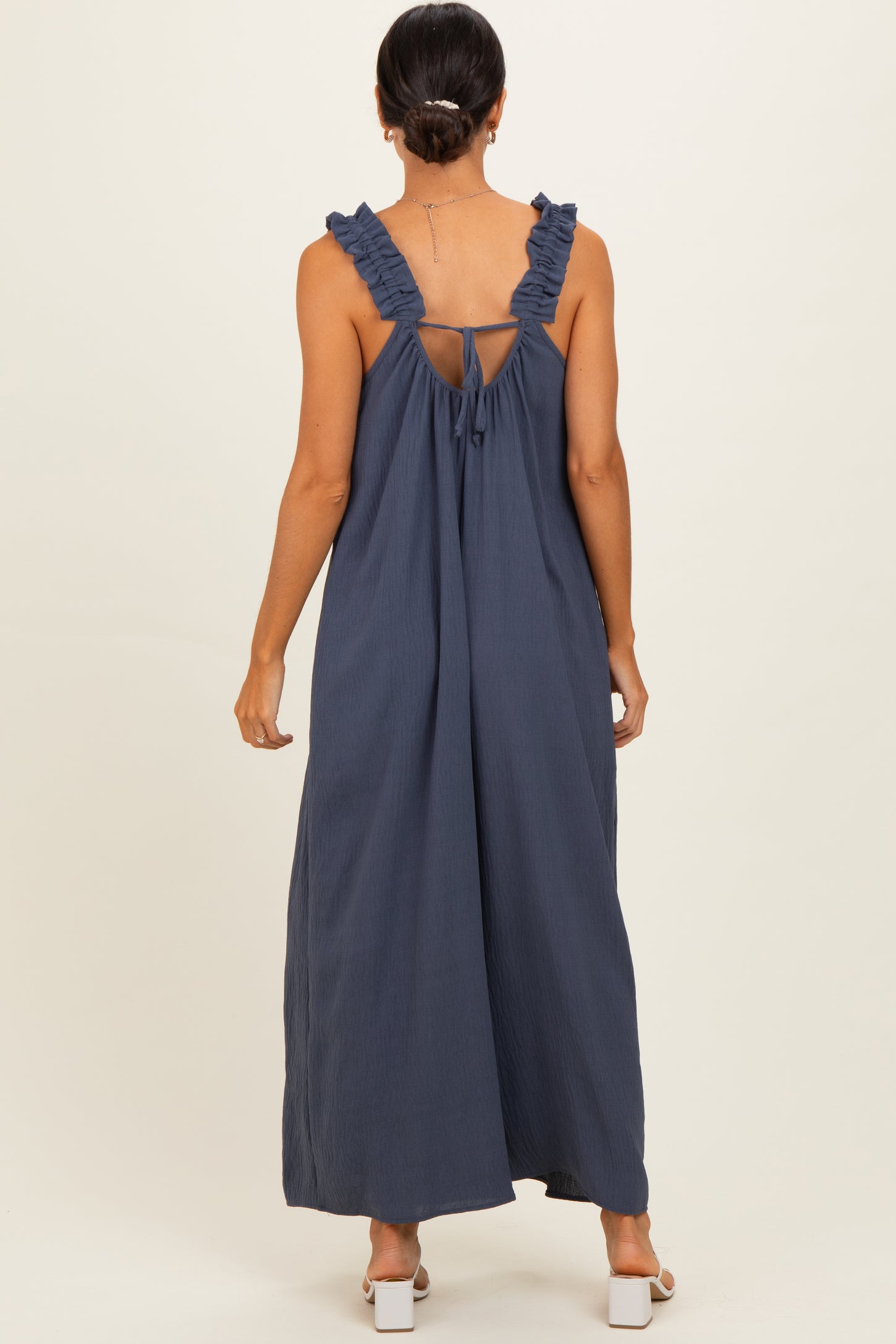 woman wearing a navy blue maxi dress with ruffled straps and an open back