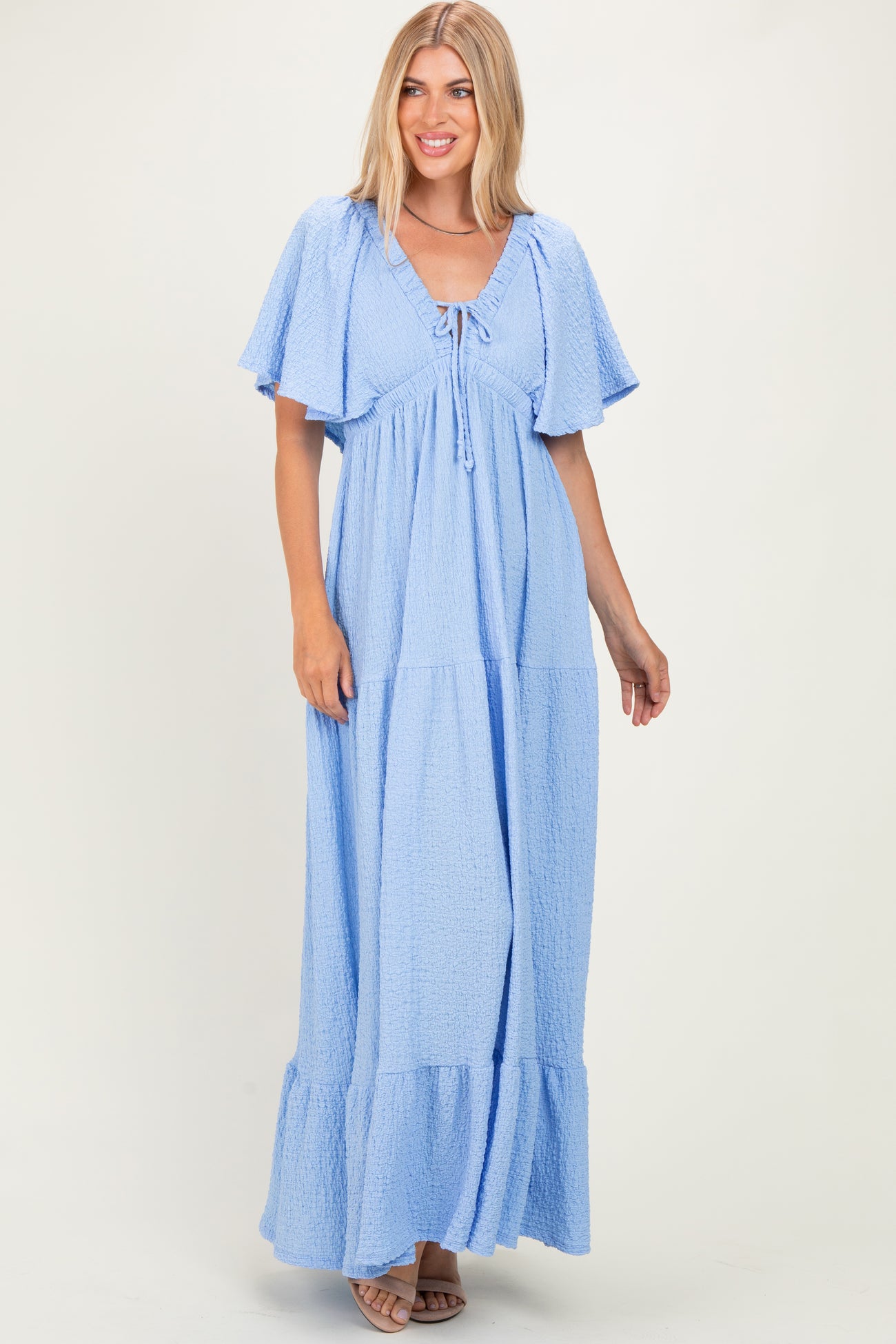 woman wearing a light blue maxi dress with flutter sleeves and a tie detail at the neckline