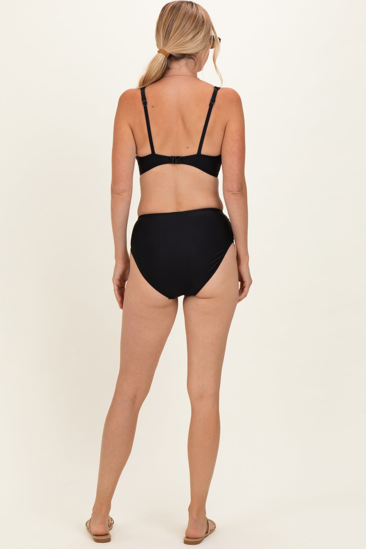 woman wearing a black two-piece bikini set with a high-waisted bottom and adjustable straps, seen from the back